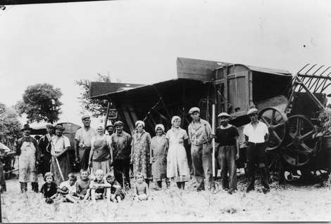 Das Bild zeigt die Frauen, Männer und Kinder vor der großen Dreschmaschine.
